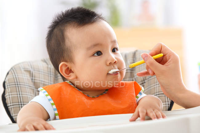 Partial view of mother holding spoon and feeding adorable little baby — Stock Photo