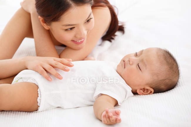 Молода мати дивиться на чарівну дитину, яка спить на ліжку — стокове фото