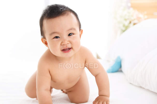 Carino felice asiatico bambino ragazzo strisciando su letto e guardando fotocamera — Foto stock