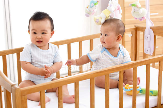Two adorable babies boys sitting together in crib — Stock Photo
