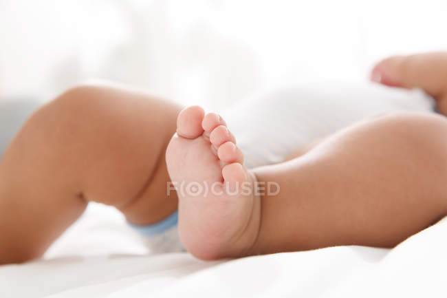 Vista de cerca de pequeños pies de lindo bebé acostado en la cama - foto de stock
