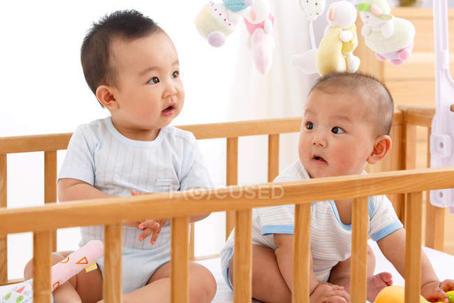 Two adorable babies boys sitting together in crib — Stock Photo