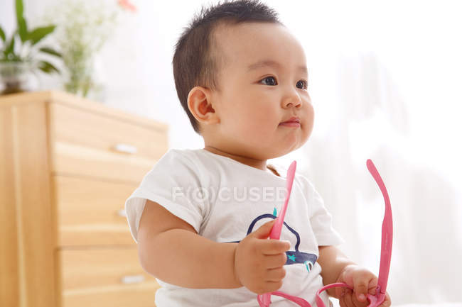 Cute asian baby boy holding pink eyeglasses and looking away — Stock Photo