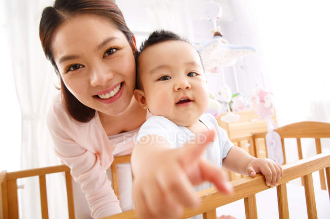 Happy young mother playing with adorable little baby in crib, selective focus — Stock Photo