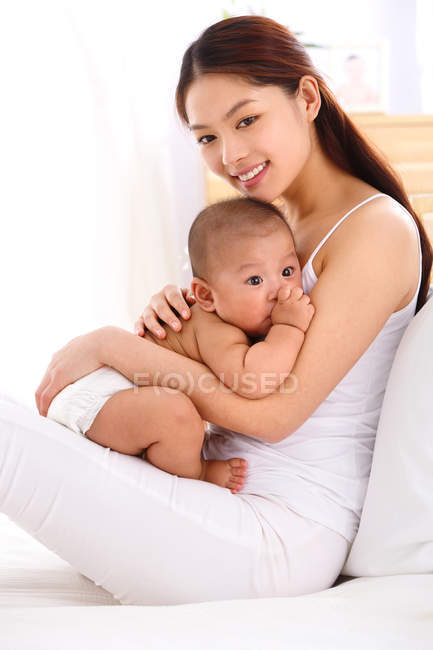 Heureuse jeune mère étreignant adorable petit bébé à la maison — Photo de stock