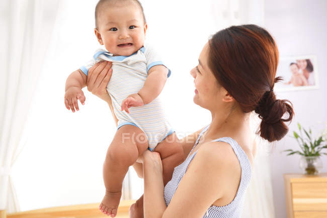 Feliz jovem asiático mãe segurando adorável pouco bebê em casa — Fotografia de Stock
