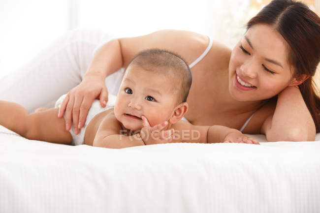Glückliche junge Mutter mit süßem Baby zu Hause im Bett liegend — Stockfoto
