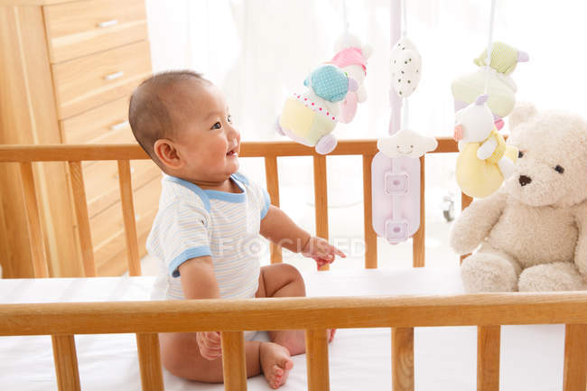 Visão de alto ângulo de adorável bebê feliz sentado no berço e olhando para brinquedos — Fotografia de Stock