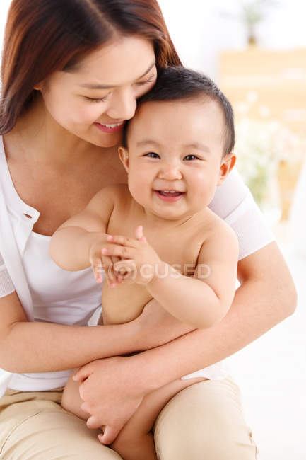 Feliz joven madre abrazando adorable pequeño bebé en casa - foto de stock