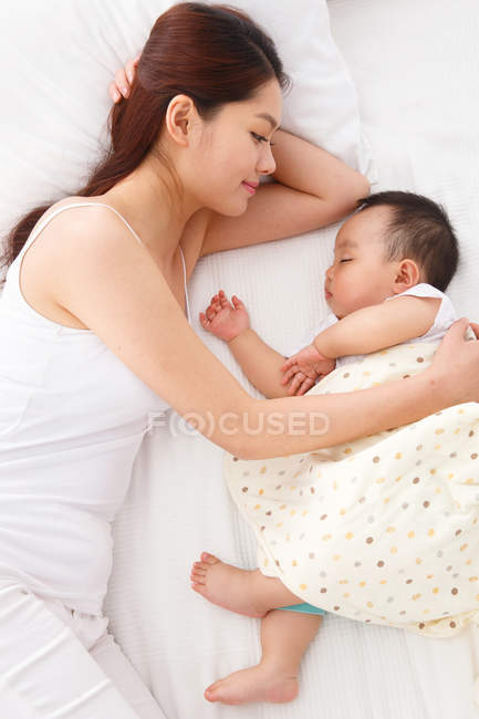 Blick von oben auf junge Mutter, die ihr entzückendes Baby ansieht, das auf dem Bett schläft — Stockfoto