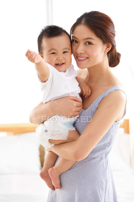 Щаслива молода мати тримає чарівну дитину і посміхається на камеру — стокове фото