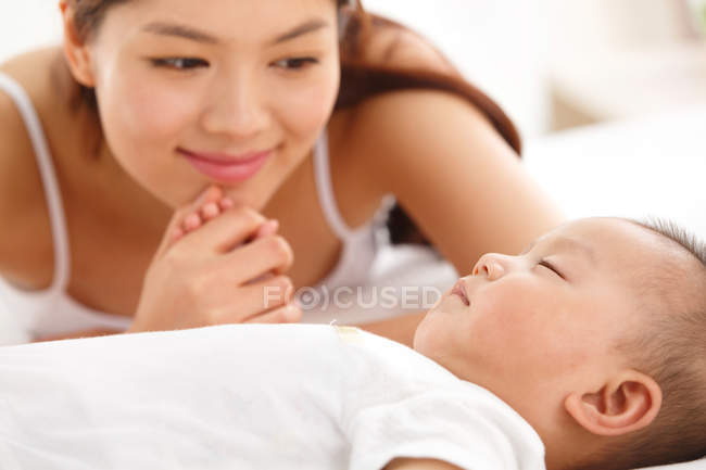 Молодая мать смотрит на восхитительного ребенка, спящего на кровати — стоковое фото