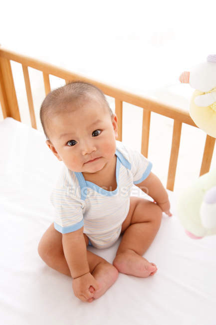High angle view of adorable asian baby boy sitting in crib and looking at camera — Stock Photo