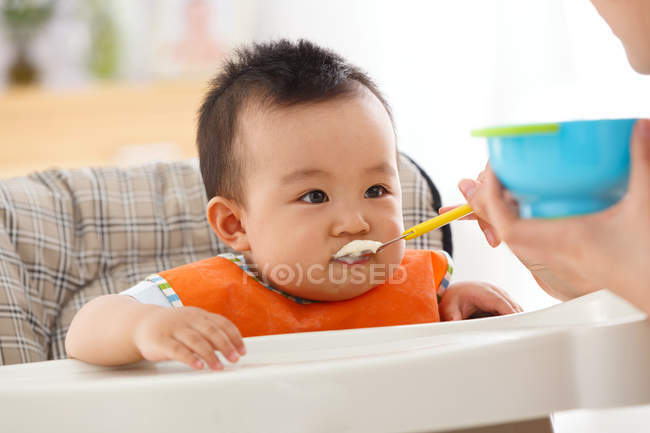 Tiro cortado de mãe segurando colher e alimentação adorável bebê pequeno — Fotografia de Stock