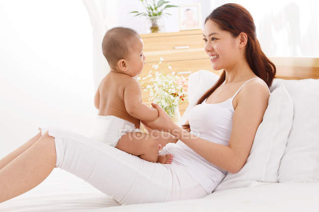 Feliz joven asiático madre jugando con adorable poco bebé en casa - foto de stock