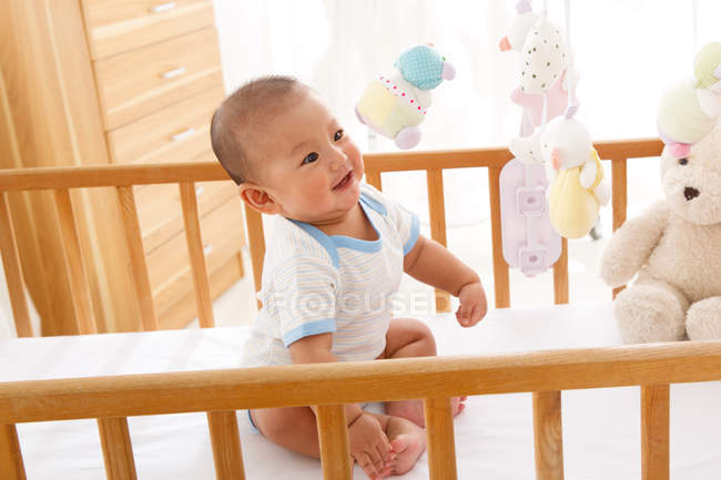 High angle view of adorable happy chinese baby boy sitting on crib — Stock Photo