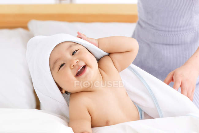 Recortado disparo de la madre de pie cerca adorable feliz bebé acostado en la cama - foto de stock