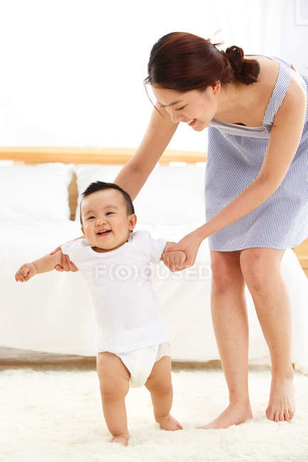 Feliz jovem mãe aprendendo adorável pequeno bebê para andar em casa — Fotografia de Stock