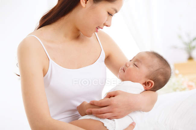 Feliz joven madre llevando adorable pequeño bebé en casa - foto de stock