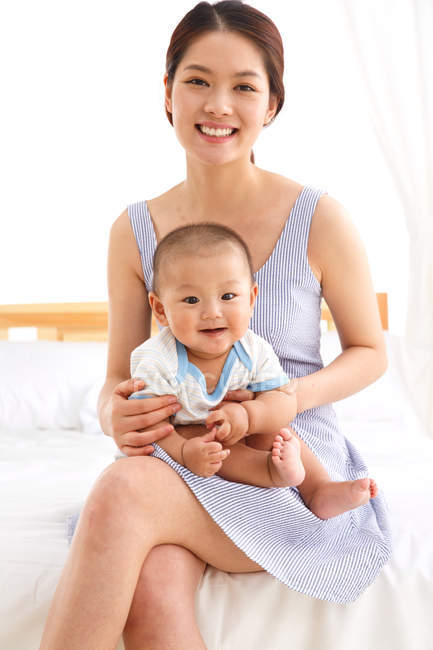 Feliz joven asiático madre holding adorable poco bebé en casa - foto de stock