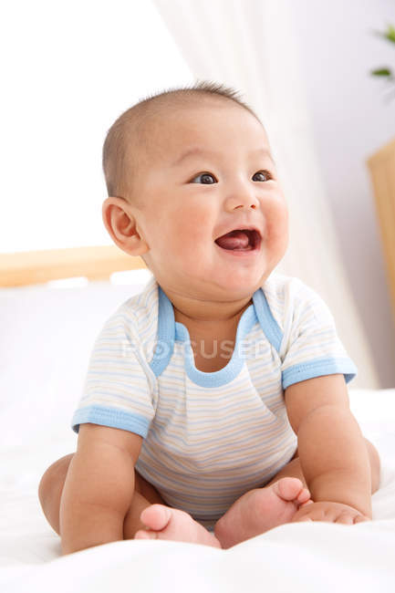 Close-up vista de adorável menino chinês feliz sentado na cama — Fotografia de Stock