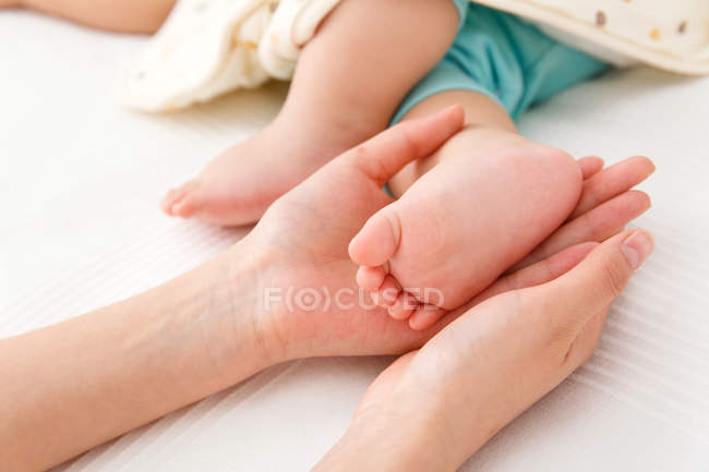 Primer plano vista parcial de la madre sosteniendo poco pie de su bebé - foto de stock
