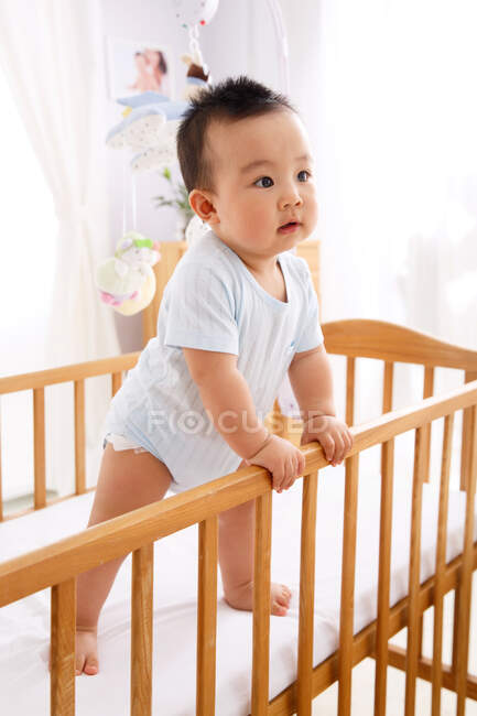 O bebê está de pé sobre a pequena cama. — Fotografia de Stock