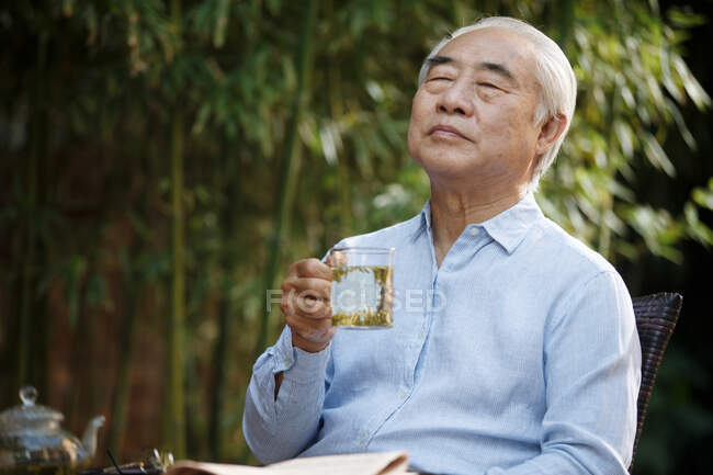 Старший чоловік сидить у дворі п'є чай — стокове фото