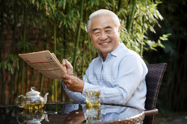 Senior man sitting in yard drinking tea — Stock Photo