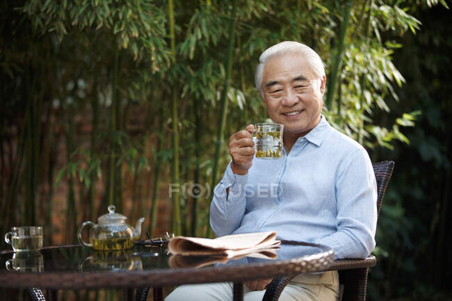 Hombre mayor sentado en el patio bebiendo té - foto de stock