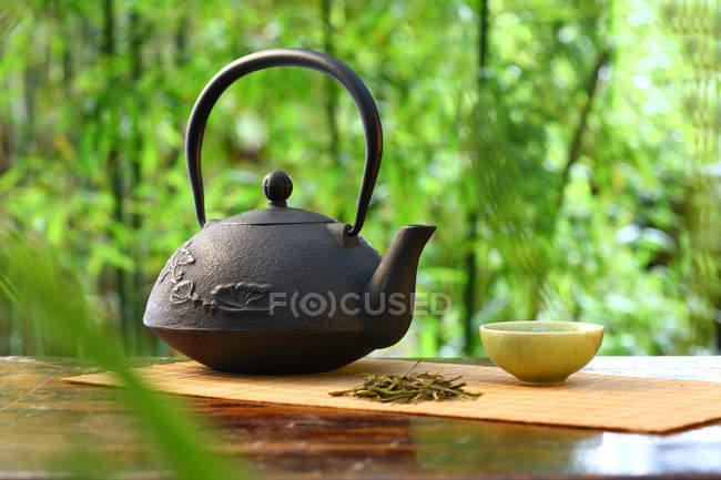Vista de primer plano del juego de té clásico chino en la mesa de madera con plantas de bambú borrosas, enfoque selectivo - foto de stock