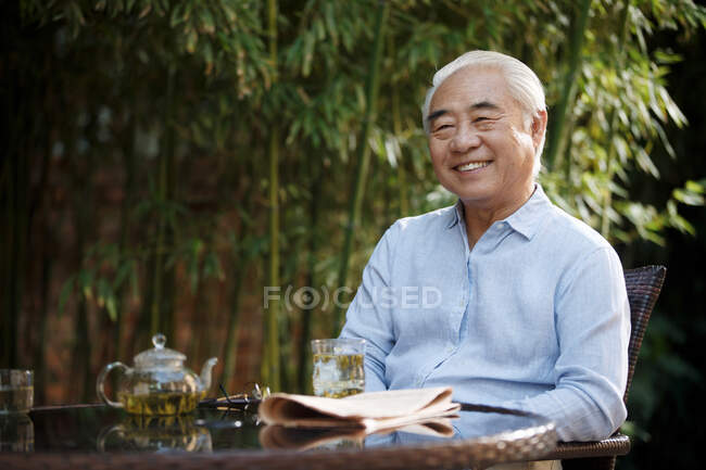 Hombre mayor sentado en el patio bebiendo té - foto de stock