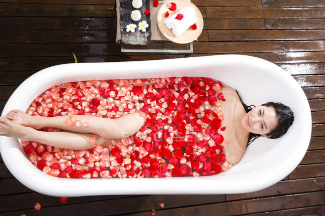 Vista superior de hermosa mujer joven sonriente lavándose en baño de pétalos al aire libre - foto de stock