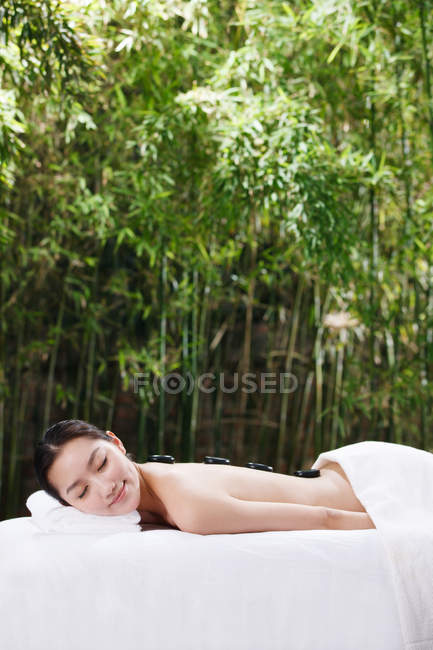 Sonriente joven asiática mujer con los ojos cerrados acostado en el spa al aire libre - foto de stock