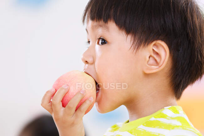 O menino está comendo uma maçã — Fotografia de Stock