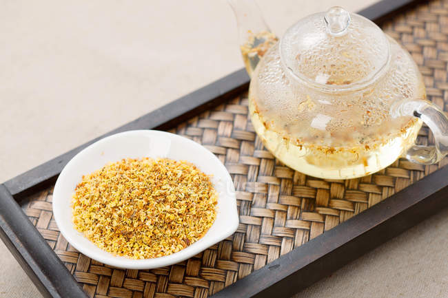 Крупным планом вид на чай Османтус в миске и стеклянный чайник на подносе — стоковое фото