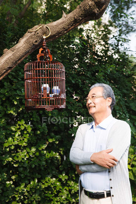 Um velho no quintal e olhou para a gaiola dos pássaros — Fotografia de Stock