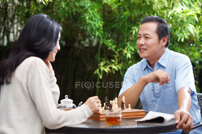 Una pareja de mediana edad jugando al ajedrez en el patio - foto de stock