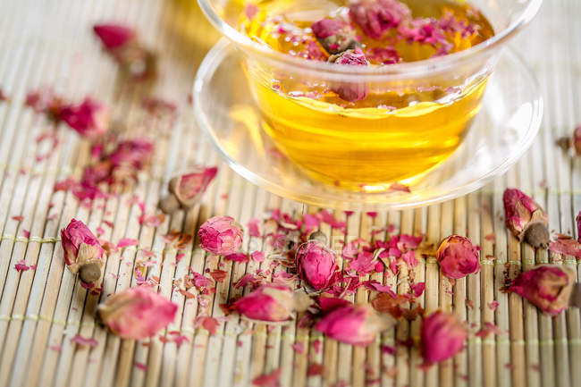 Крупный план здорового органического травяного чая в стеклянной чашке и цветах на столе — стоковое фото