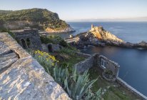 Flowers and blue sea frame the old castle and church at dawn Portovenere, UNESCO World Heritage Site, Riviera di Levante, Ligury, Italy, Europe — Stock Photo