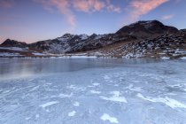 Lumières roses de l'aube sur les sommets enneigés autour de la surface gelée du lac Andossi, Vallespluga, Valtellina, Lombardie, Italie, Europe — Photo de stock