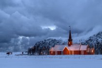 Luci sulla chiesa al tramonto con le cime innevate sullo sfondo Flakstad, Isole Lofoten, Norvegia, Europa — Foto stock