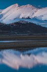 Vue de Castelluccio di Norcia devant une grande montagne enneigée et reflétée dans un lac de la vallée, Ombrie, Italie — Photo de stock