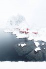 Le cime innevate e il mare ghiacciato fanno da cornice alle tipiche case dei pescatori chiamate Rorbu Hamny Lofoten Islands Norvegia settentrionale Europa — Foto stock