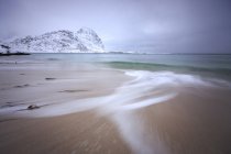 Ondas do mar gelado na praia no fundo os picos nevados Pólen Vareid Flakstad, Lofoten Islands landscape, Noruega, Europa — Fotografia de Stock