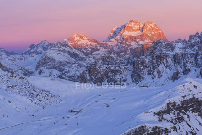 La carretera que va a Passo Giau durante una puesta de sol de invierno, en el fondo Sorapiss iluminado por los últimos rayos del sol al atardecer, Dolomitas, Véneto, Italia - foto de stock