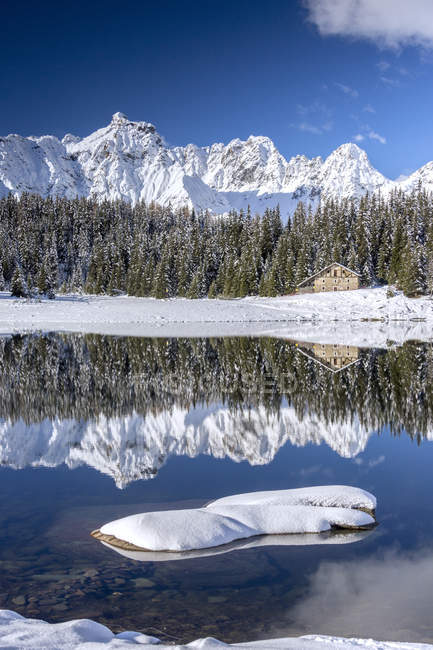 Chalé de madeira rodeado por picos nevados e madeiras refletidas na paisagem Pal Lake, Malenco Valley, Valtellina, Lombardia, Itália, Europa — Fotografia de Stock