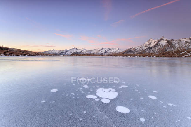 Ice bubbles on the frozen surface of Andossi Lake at sunrise, Vallespluga mountain landscape, Lombardy, Italy, Europe — Stock Photo