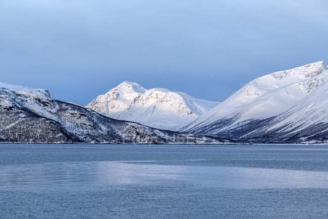 Ciel bleu et sommets enneigés entourent la mer froide Lyngen Alpes Troms, Laponie, Norvège, Europe — Photo de stock