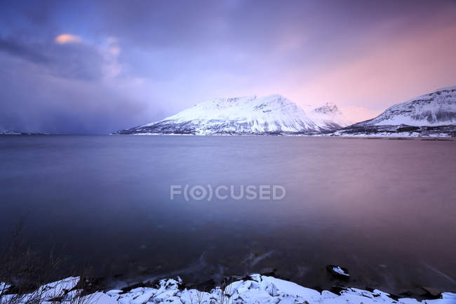 El cielo se vuelve rosado al atardecer y se refleja en el mar congelado Storfjorden Laponia Lyngen Alpes Troms Noruega paisaje, Europa - foto de stock